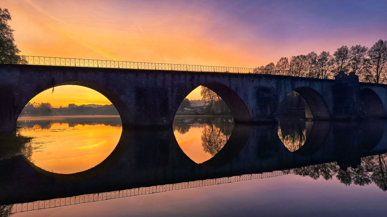 Stone bridge arches reflected in a river at sunset